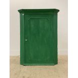 A George III green painted oak wall hanging corner cabinet, the dentil cornice above a panelled door