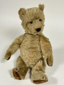 A 1920s golden mohair straw filled teddy bear with inset glass eyes, stiched nose and mouth and