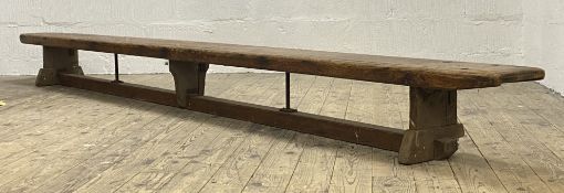 An early 20th century school bench, the plank top on three panel supports united by a floor