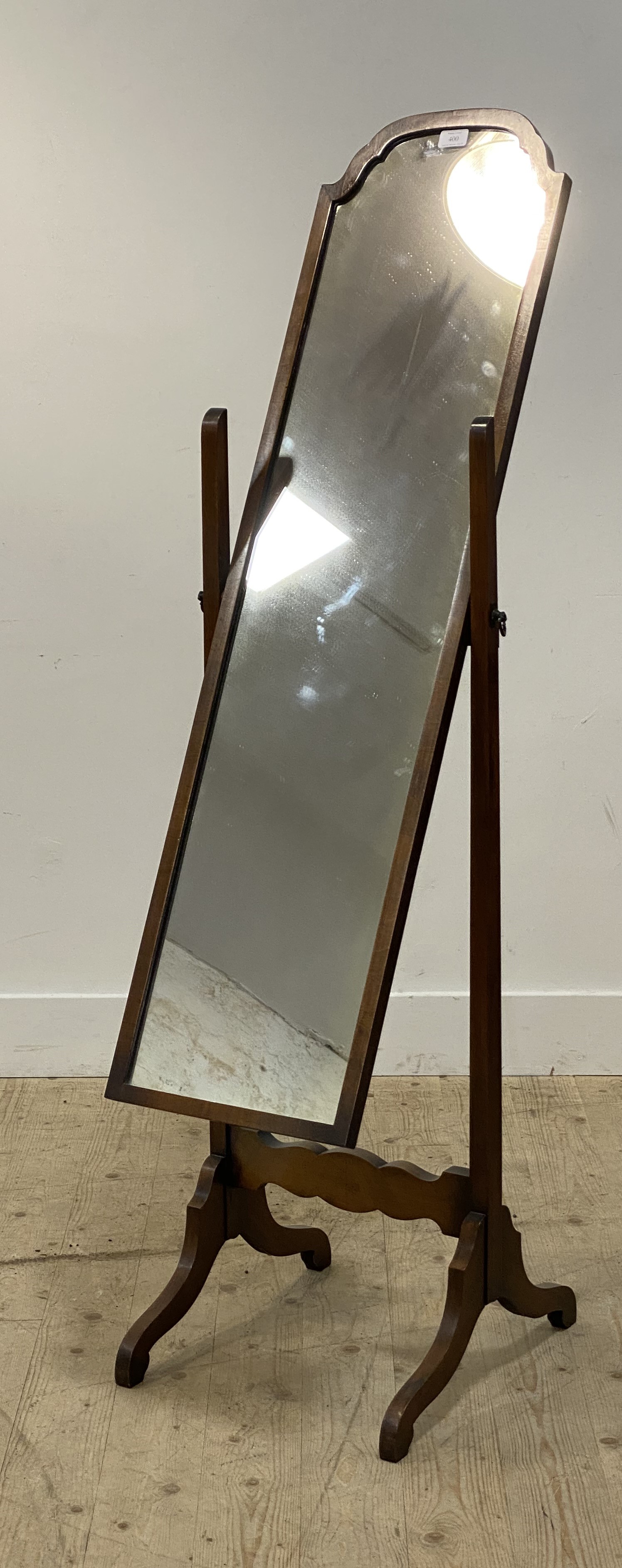 An early 20th century walnut cheval mirror, the rectangular plate with undulating top swivelling