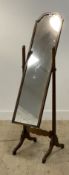 An early 20th century walnut cheval mirror, the rectangular plate with undulating top swivelling