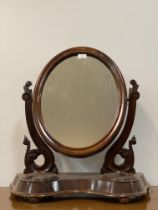 A Victorian mahogany vanity mirror, the oval mirror swivelling between two floral carved uprights,