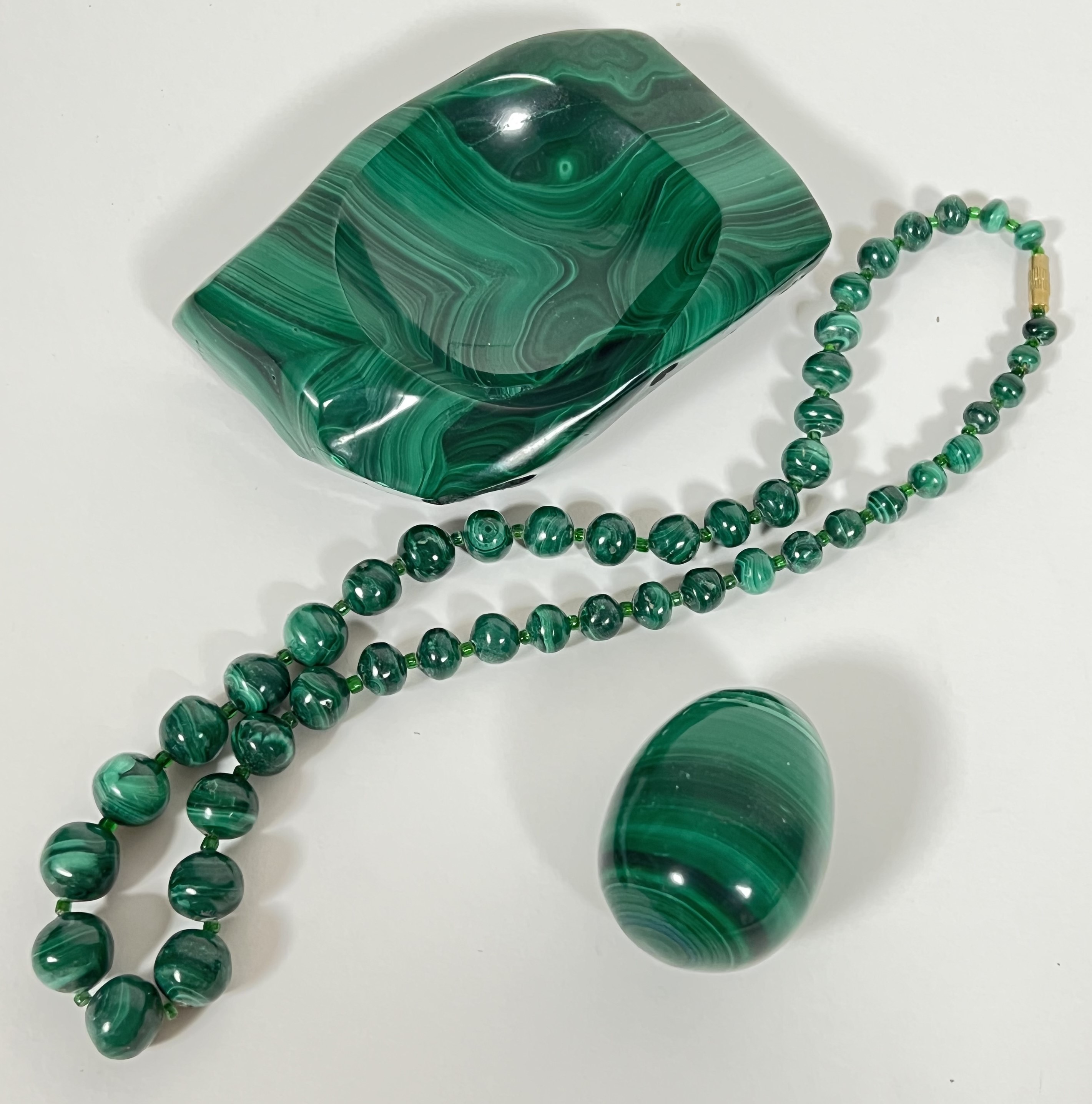 A group of malachite items comprising a beaded necklace, a carved pin dish and a turned egg (3)