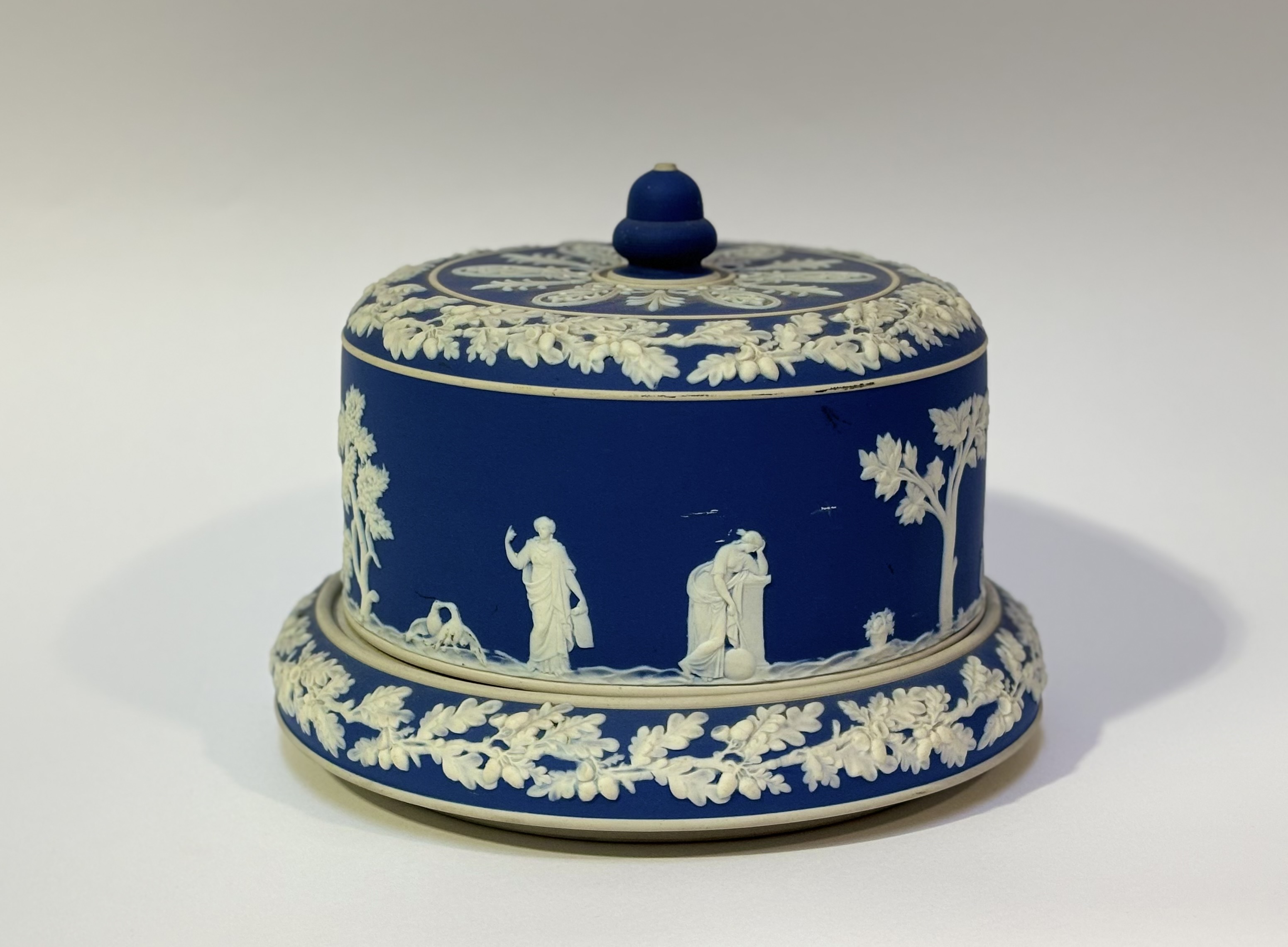 A Jasperware dark blue cheese dome decorated with classical figures. (marked K) (h-20cm w-26cm)