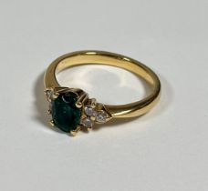 An emerald and diamond cluster ring, the oval-cut emerald claw-set between twin groups of three