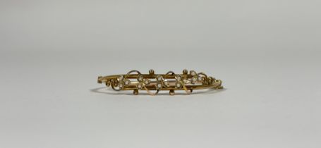 An Edwardian gold (unmarked) and seed pearl hinged bangle, set to one half with open scrollwork