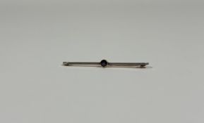 A 15ct gold bar brooch set with a sapphire, the knife-edge bar set to the centre with a millegrain-