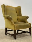 A George III mahogany wingback armchair, with undulating top and wings above out-swept arms,