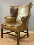 A Georgian style mahogany framed wingback armchair, upholstered in distressed tan leather