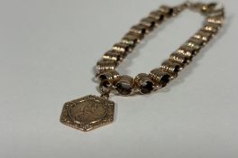 A yellow metal chainlink bracelet, of reeded shaped barrel links, unmarked, suspending a 9ct gold