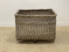 A large wicker laundry or log basket, early 20th century, with rope handle to each end and moving on
