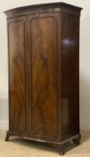 An early 20th century mahogany bow front wardrobe, the projecting cornice above two panelled doors