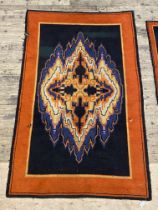 A vintage knotted rug, the black field with vibrant abstract medallion within an orange border.