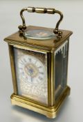 A Edwardian brass four glass clock with swing handle to top and enamel dial with roman numerals