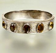 A late Victorian white metal engraved stiff hinged hollow bangle with five oval colette set