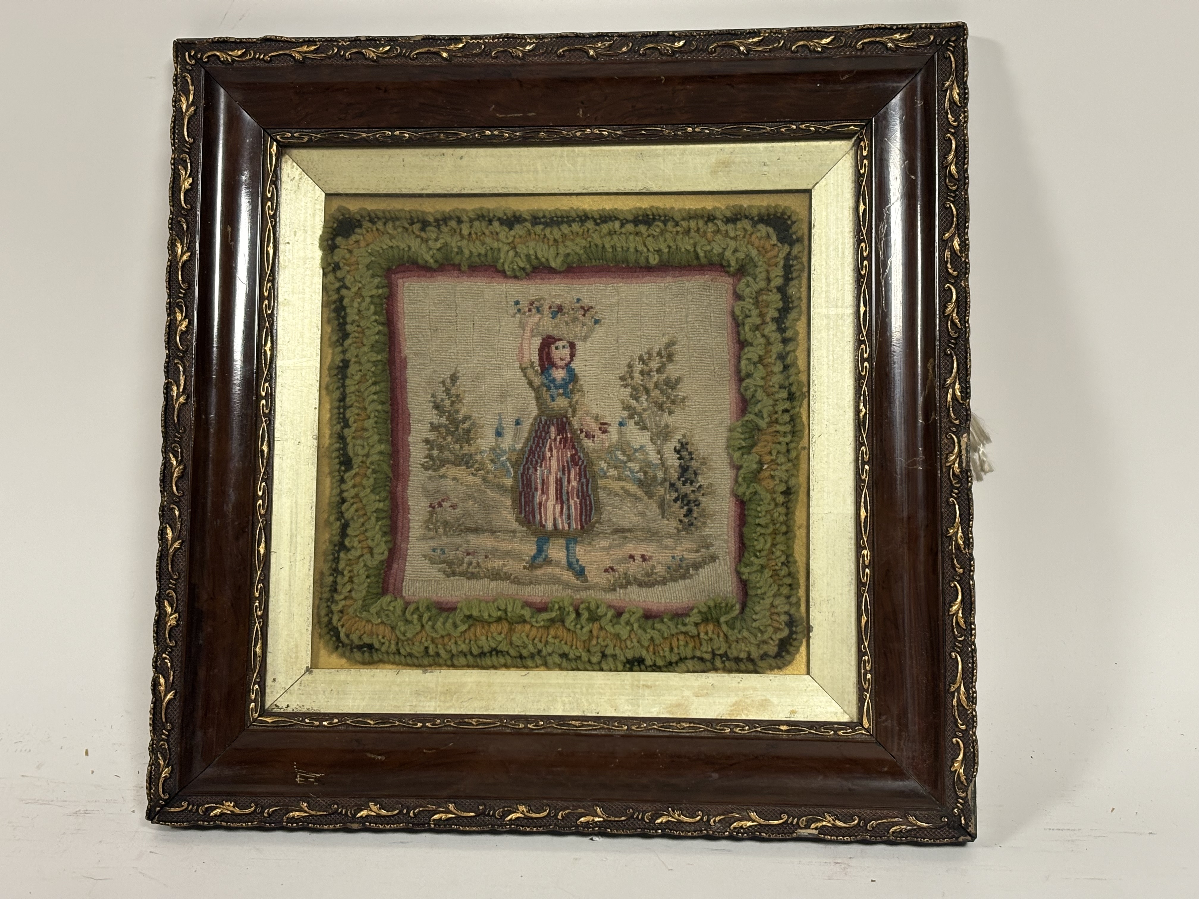 A framed embroidered textile by Catherine Caine of a woman holding a basket on her head in a field