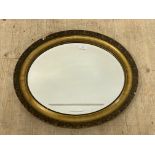 An early 20th century oval gilt composition framed wall mirror with bevelled plate. 63cm x 53cm.