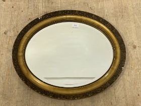 An early 20th century oval gilt composition framed wall mirror with bevelled plate. 63cm x 53cm.