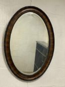 A 1920s oval walnut wall hanging mirror with ebonised beading to frame enclosing a bevelled plate