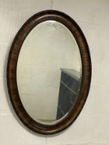 A 1920s oval walnut wall hanging mirror with ebonised beading to frame enclosing a bevelled plate