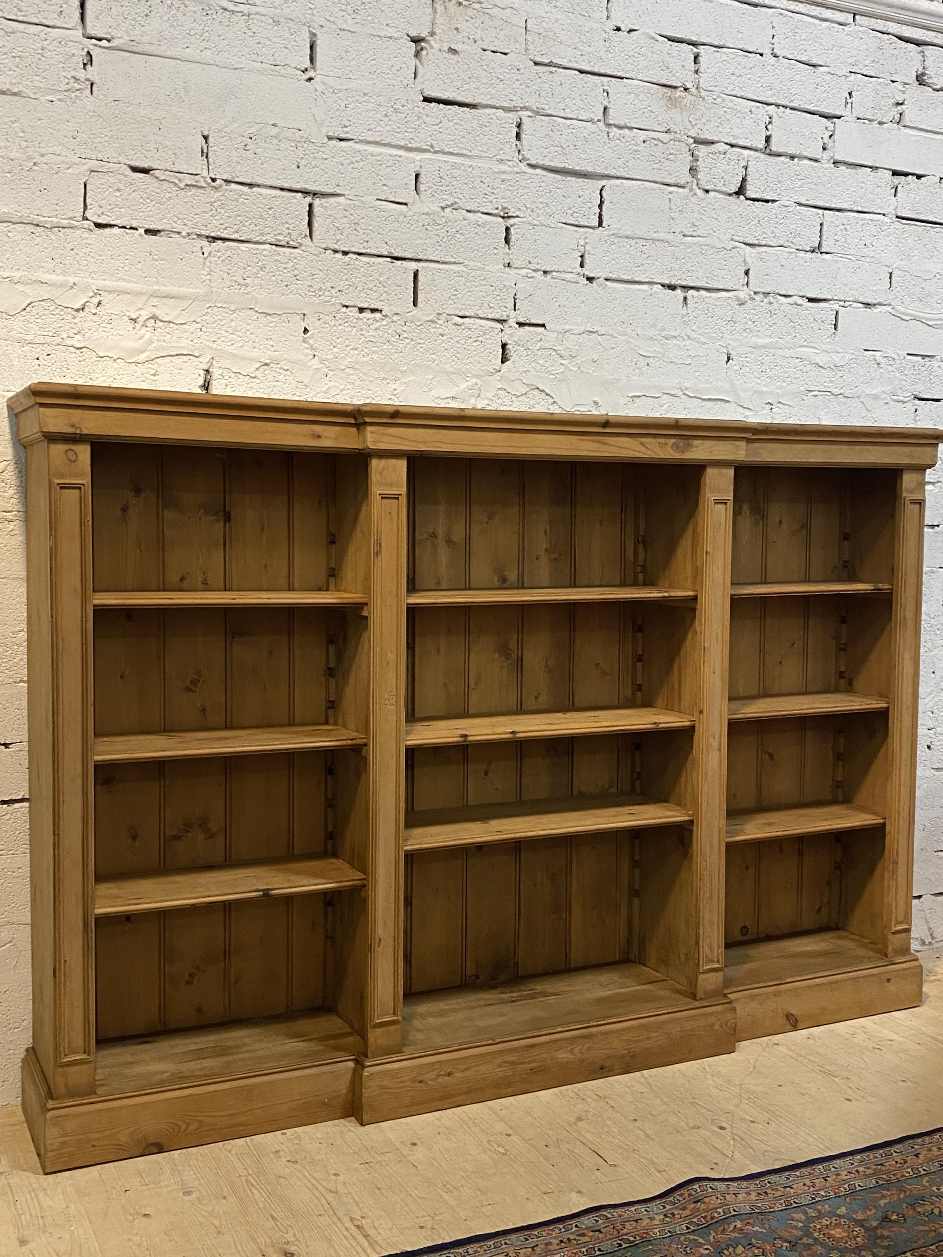 A pine breakfront bookcase, fitted with nine adjustable shelves and raised on a plinth base. H140cm,