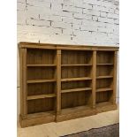A pine breakfront bookcase, fitted with nine adjustable shelves and raised on a plinth base. H140cm,