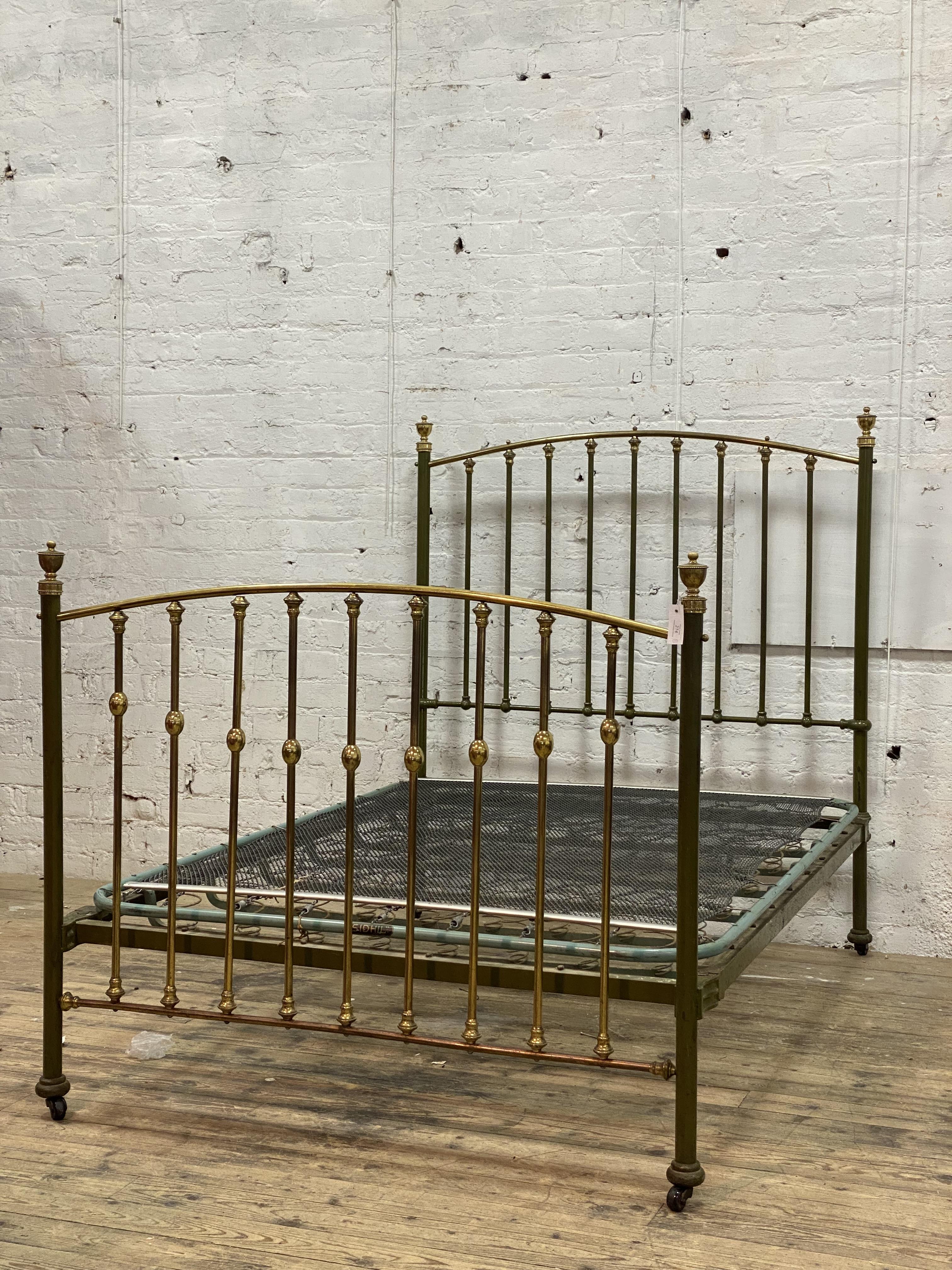 An Edwardian brass and green lacquered double bed frame, with urn finials, sprung base and moving on