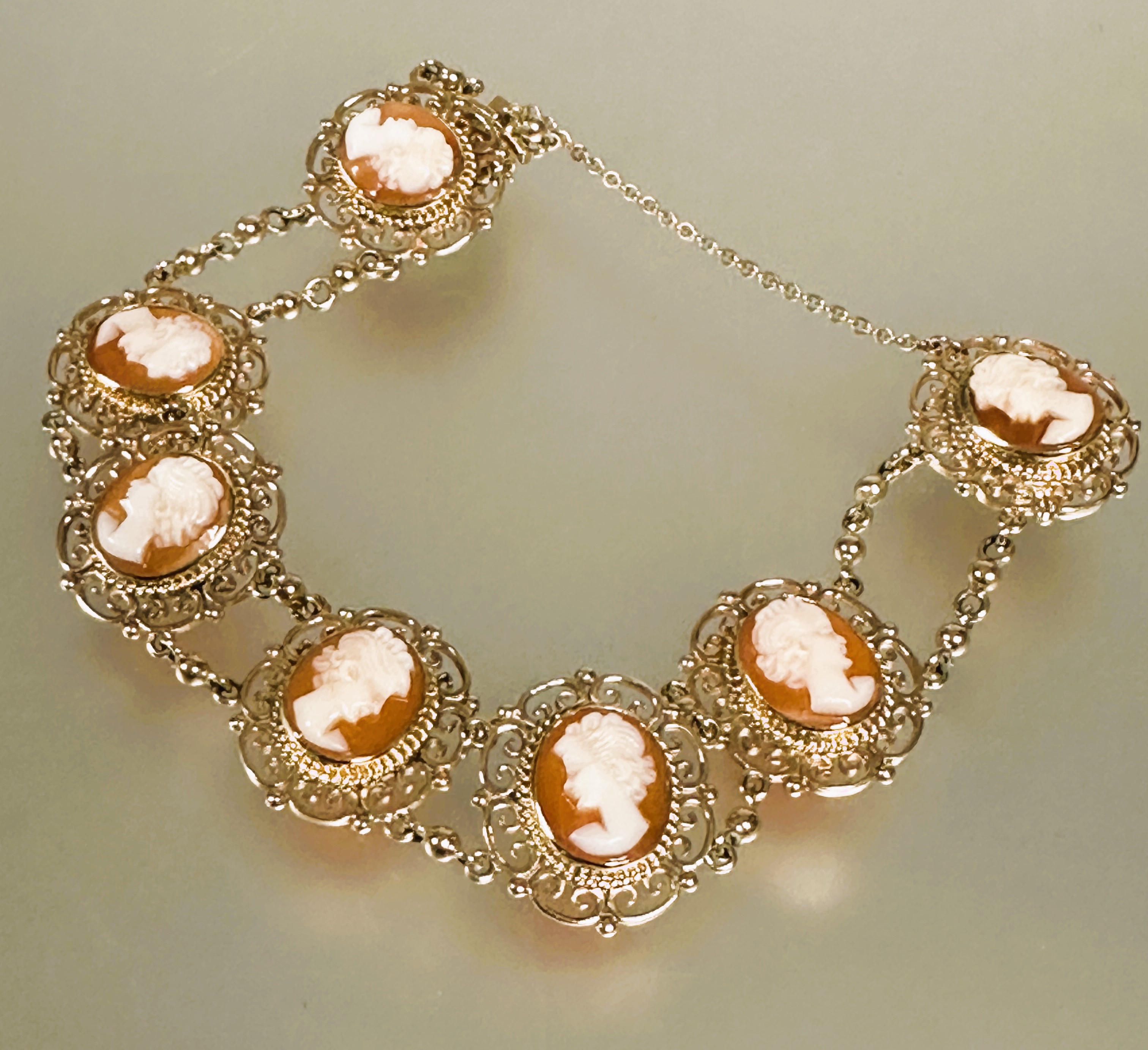 A 9ct gold bracelet set seven shell carved cameos in scrolling open work setting between chain