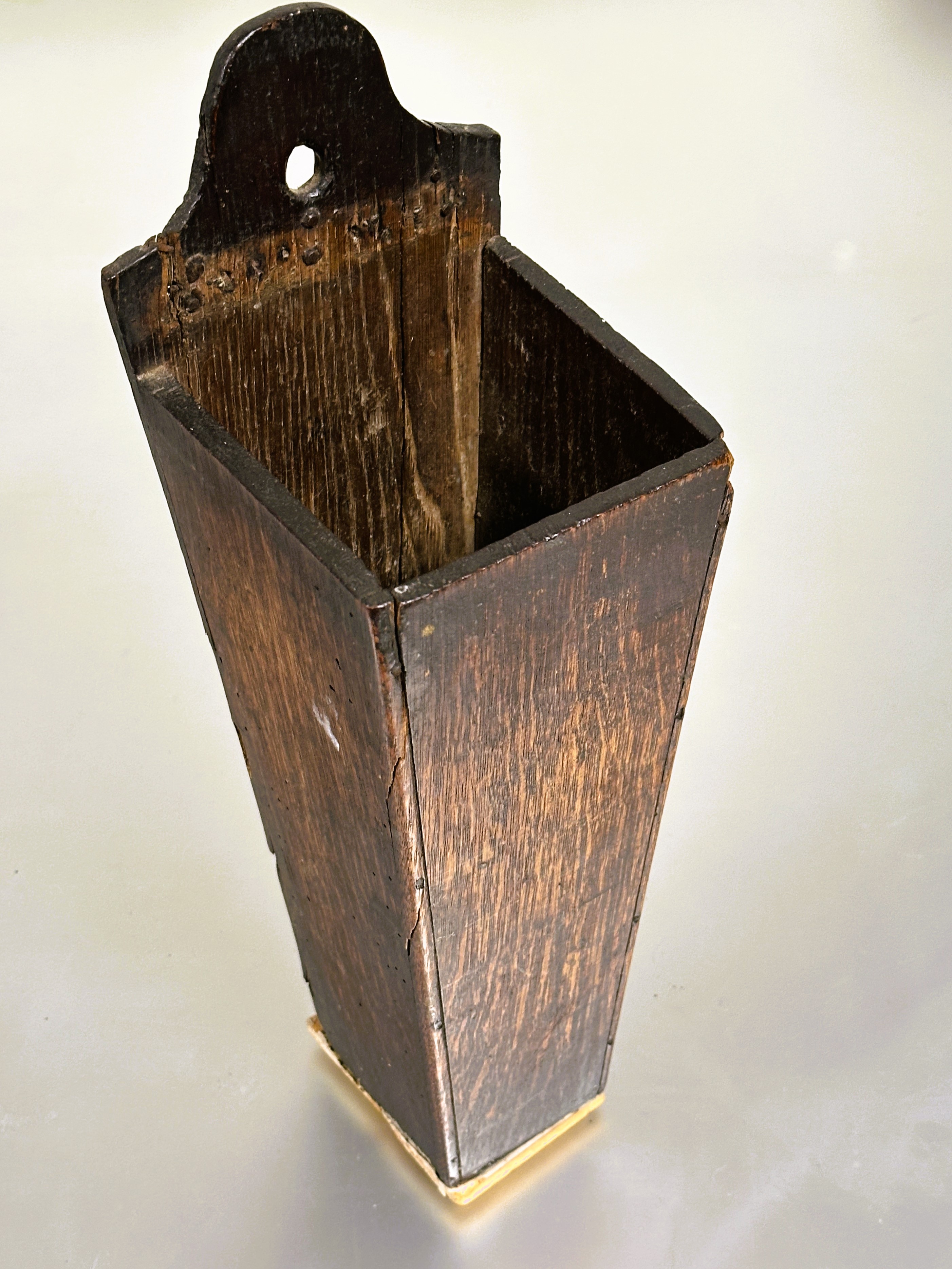 A 18thc oak candle box of tapered form with arched panel back with pierced hole and replaced base
