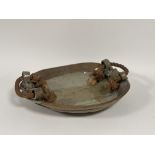 A large decorative stoneware pottery bowl with twisted hemp rope handles to side with green/brown