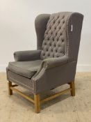 A contemporary wingback chair, upholstered in buttoned grey linen embellished with studded border,