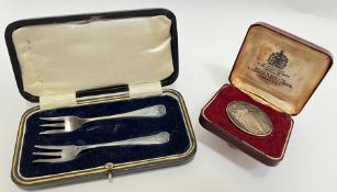 A boxed pair of hallmarked silver pickle forks, and a commemorative Churchill 1874-1965 coin