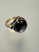 A 14ct gold ring of scrolling design with dark gray star sapphire, table rubbed, mounted in four