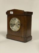 An early 20th century mantel clock in an inlaid oak case, the silvered dial with Roman chapter ring,