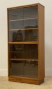 A mid century teak two height bookcase, fitted with sliding glass doors enclosing a combination of