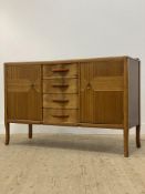 A mid century teak, mahogany, and walnut sideboard, fitted with four drawers flanked by a cupboard
