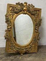 An ornate gilt composition wall hanging mirror in the Baroque taste, the oval mirror enclosed by a