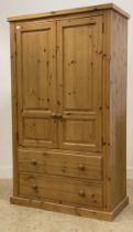 A polished pine two door wardrobe, the interior fitted for hanging and with two drawers to base.