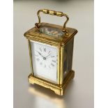 A modern brass four glass clock with folding carry handle to top white enamel dial with roman