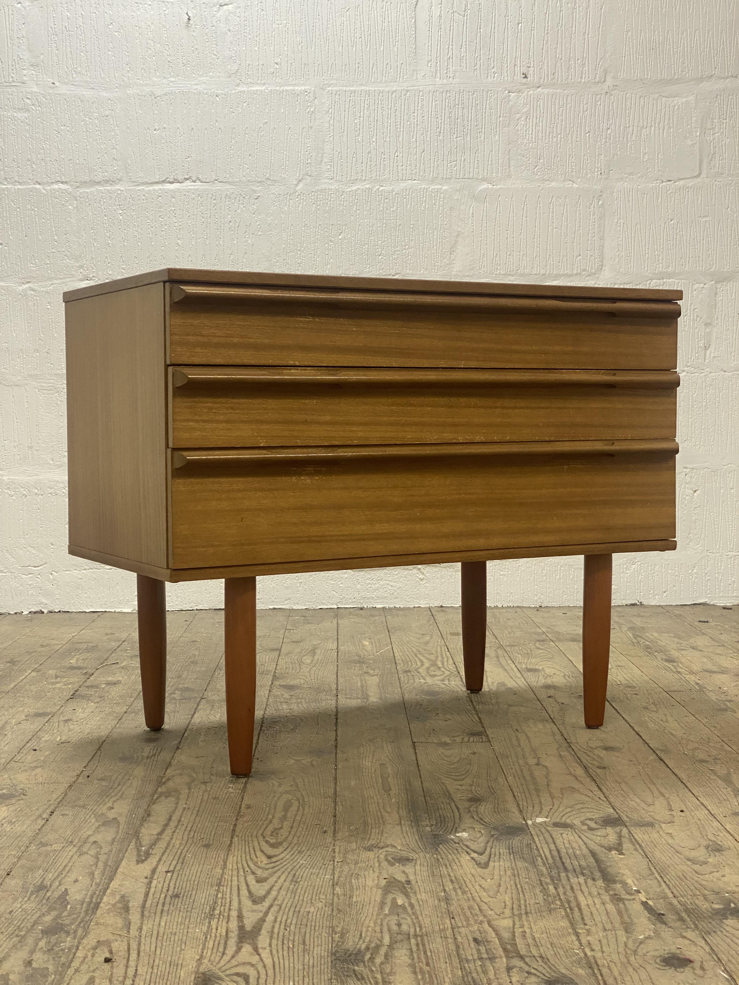 A mid century teak chest, fitted with three drawers and standing on turned and tapered supports.