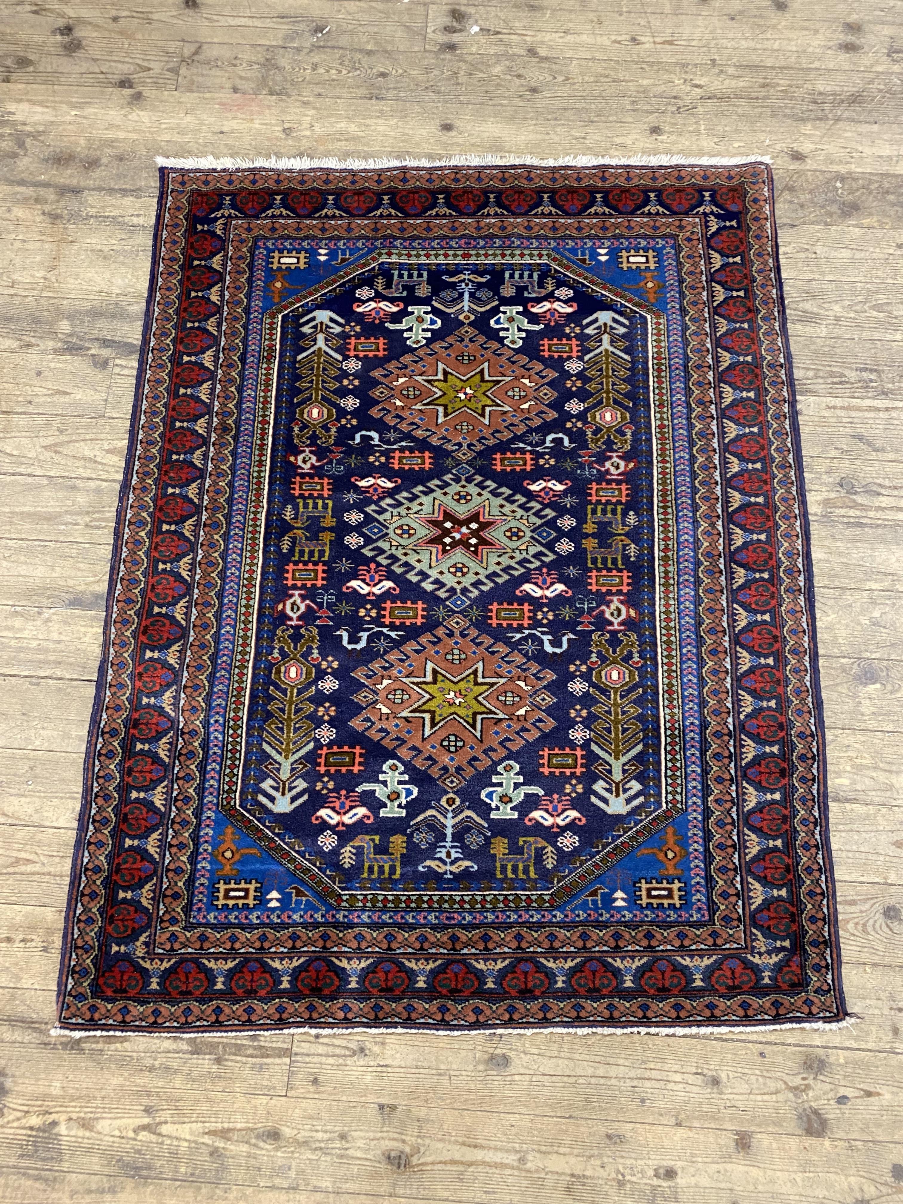A hand knotted Persian rug, the blue field decorated with pictorial motifs within a guarded