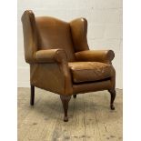 A wingback armchair, well upholstered in brown / tan leather, and raised on cabriole front supports.