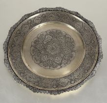 A Middle Eastern white metal scalloped serving dish with chased border enclosing a repeating lotus