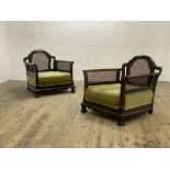 A pair of 1920's walnut bergere chairs, each with arched crest above cane back and sides, raised