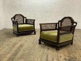 A pair of 1920's walnut bergere chairs, each with arched crest above cane back and sides, raised