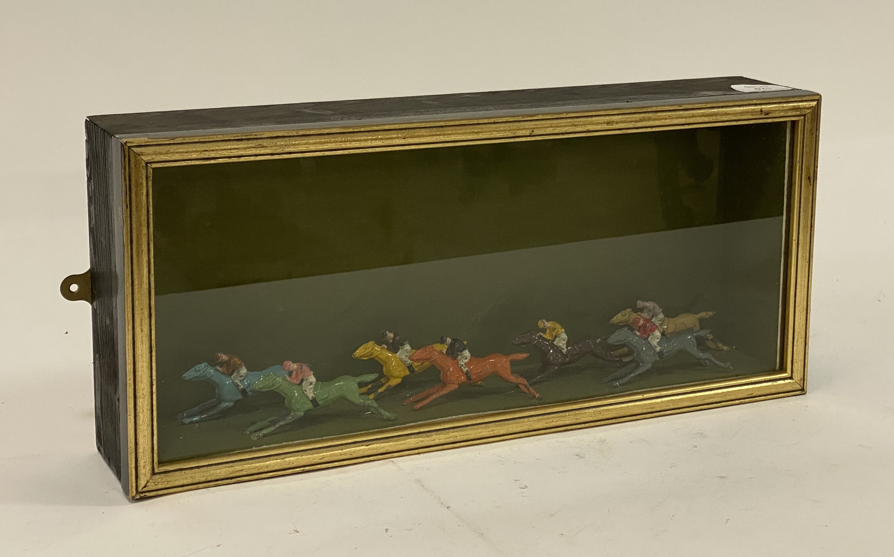An ebonised and parcel gilt glazed display case enclosing seven early 20th century lead painted
