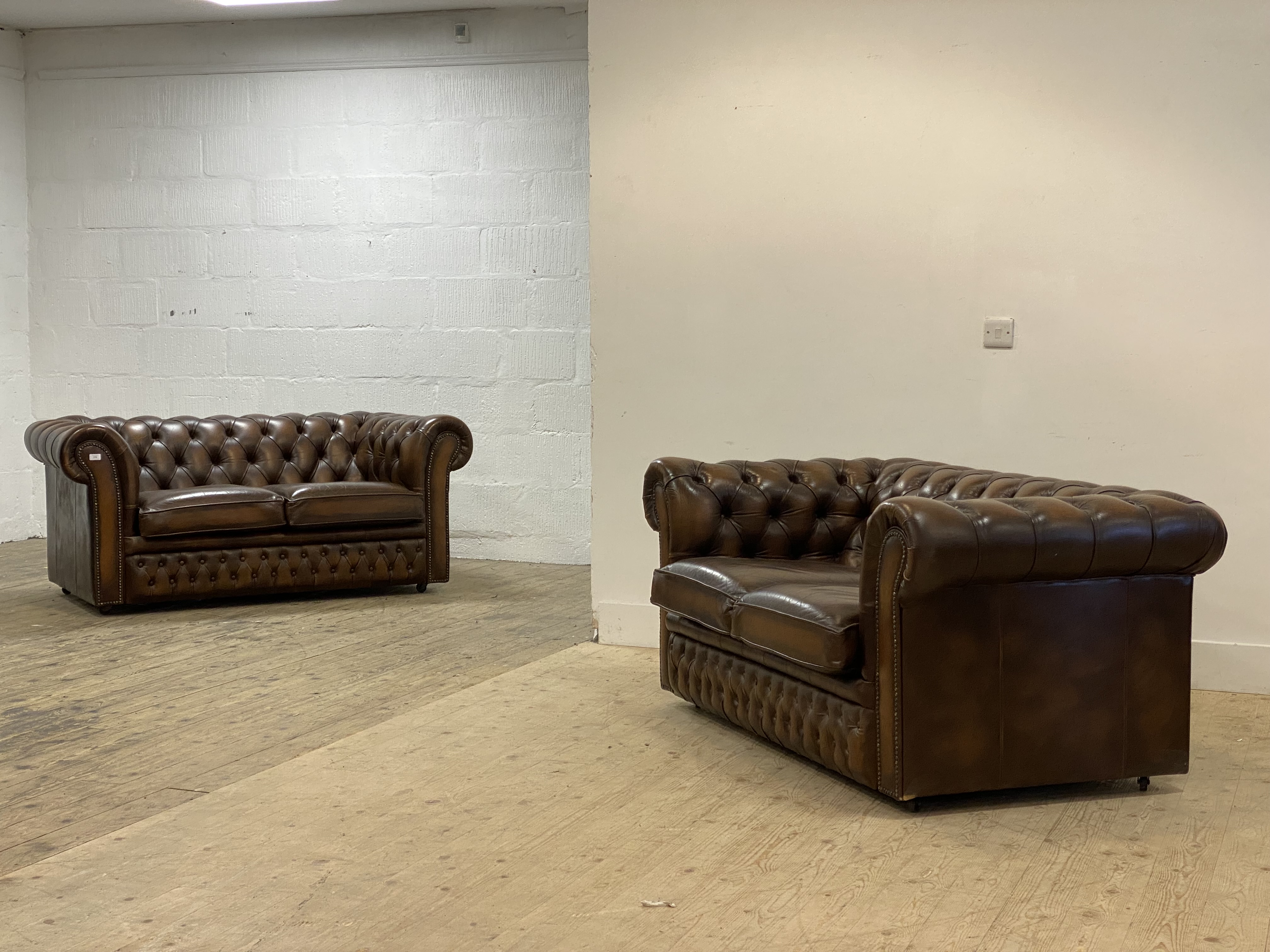 A pair of Vintage Chesterfield sofas, each upholstered in deep buttoned brown leather, moving on