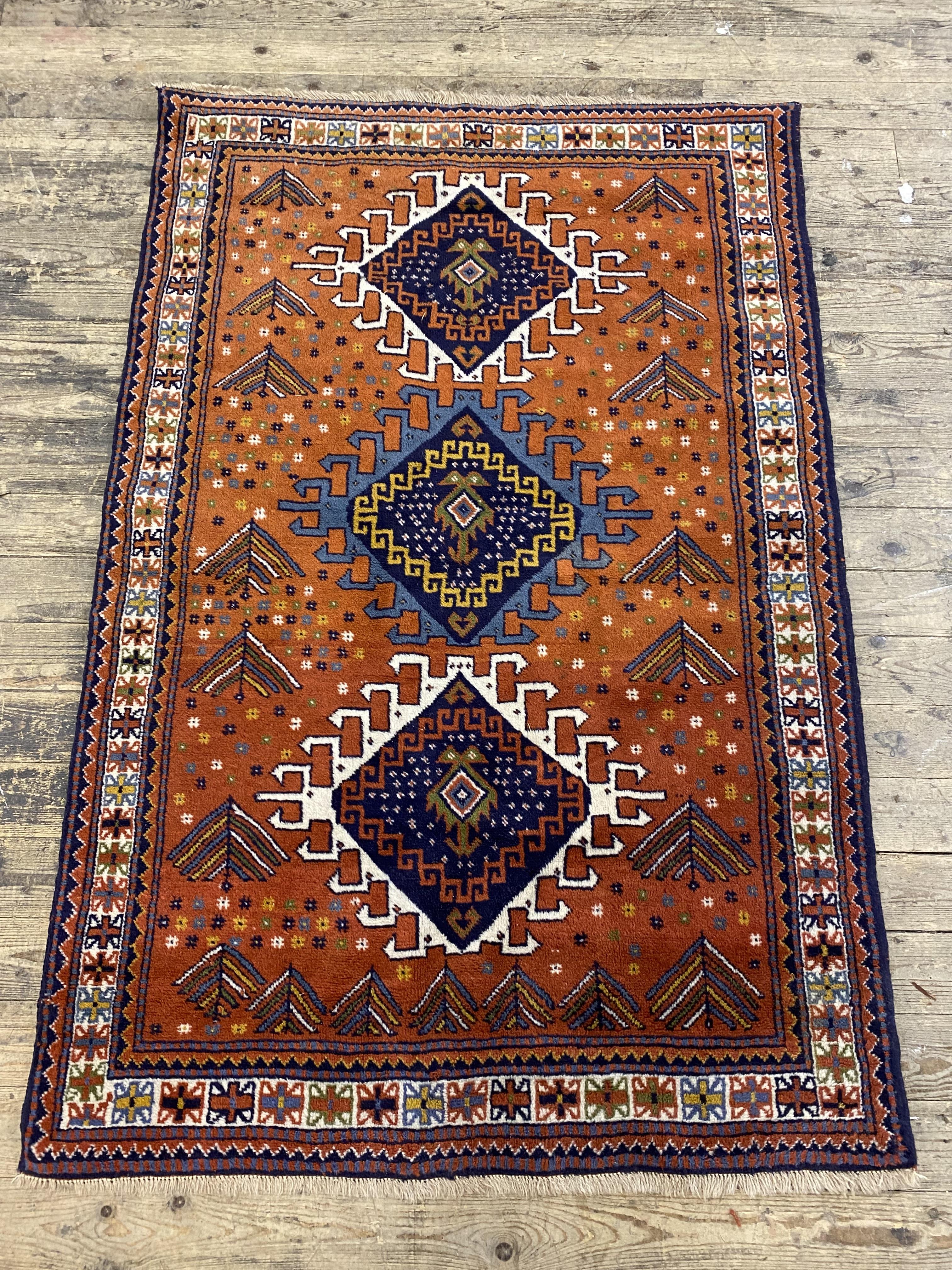 A hand knotted Kurdish rug, the madder ground with three lozenge medallions within a guarded border.
