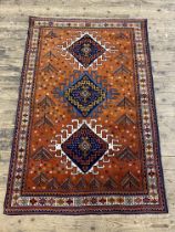 A hand knotted Kurdish rug, the madder ground with three lozenge medallions within a guarded border.