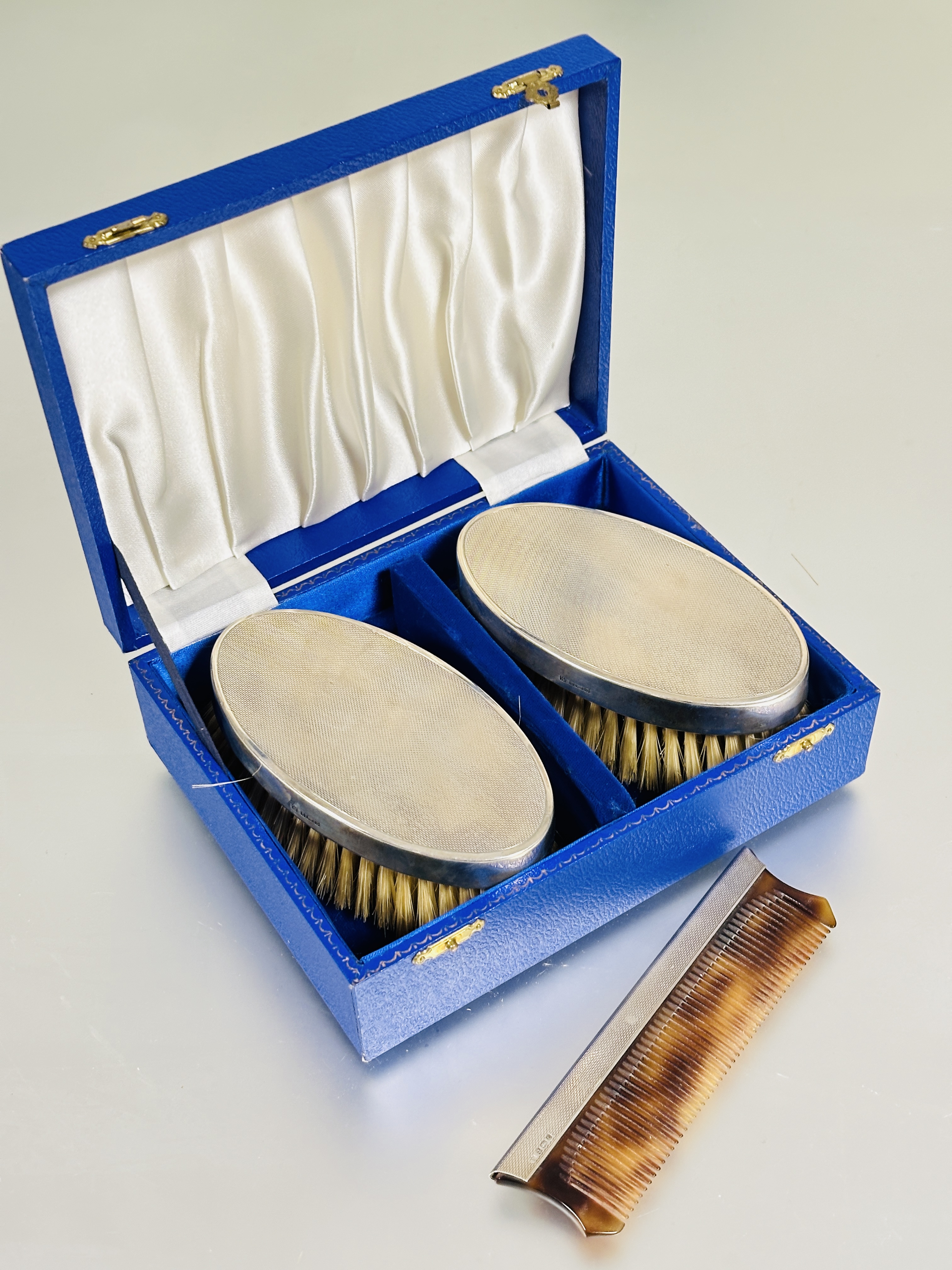 A fitted case containing a pair of Birmingham silver backed oval hair brushes with natural